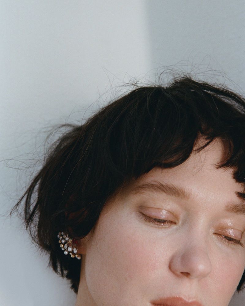 Close-up portrait of Lea Seydoux with short dark hair and an ornate pearl ear cuff against a plain white background
