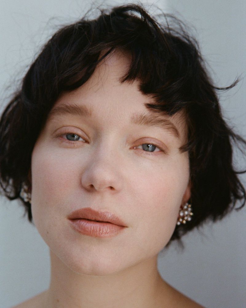 Close-up portrait of actress Léa Seydoux with short dark hair and natural makeup against a neutral backdrop.