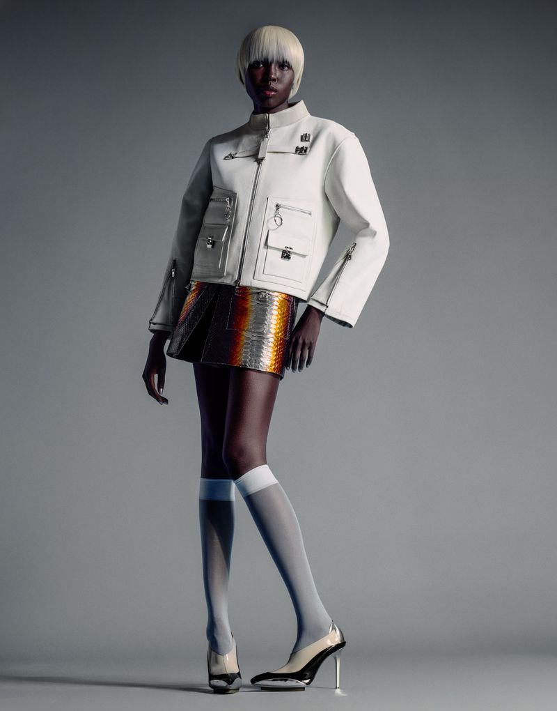 Model Ajok Madel wearing a white utility jacket and patterned miniskirt against a plain grey studio backdrop
