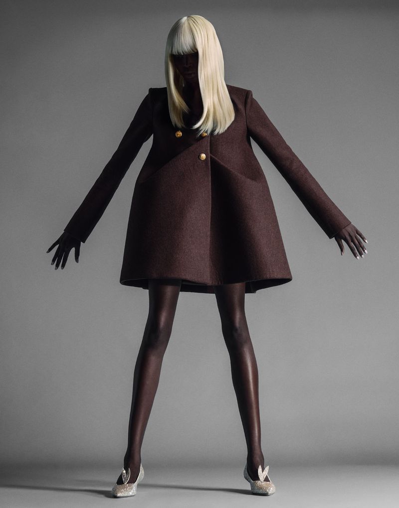 Model wearing a brown coat and platinum blonde wig against a grey seamless studio background for Enfnts Terribles issue 2.