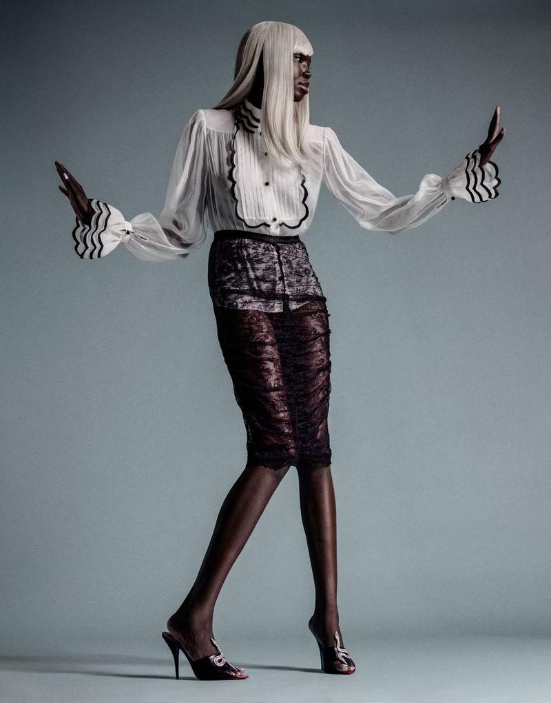 Model Ajok Madel wearing a white ruffle blouse and black lace pencil skirt against a solid grey background