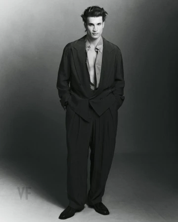 Monochrome full-length portrait of a male model wearing an oversized dark suit jacket and trousers against a gradient studio background.