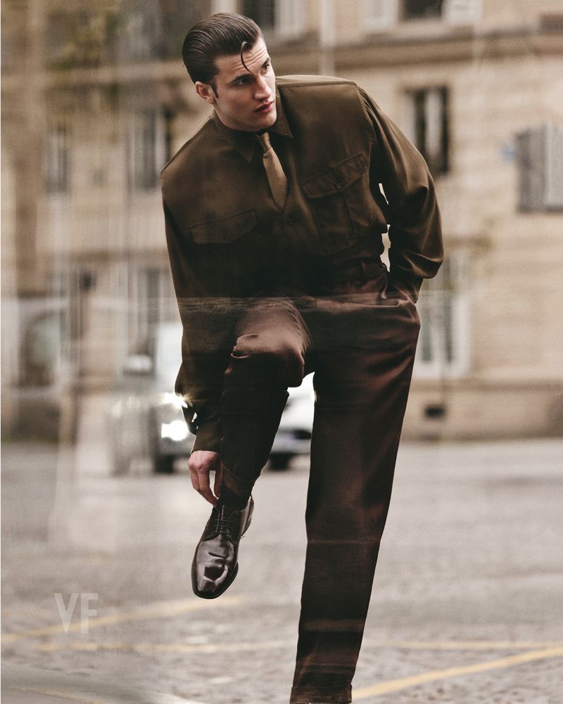 Man in brown suit posing in European city setting, glossy shoes visible in shot, fashion editorial outdoor setting, day.