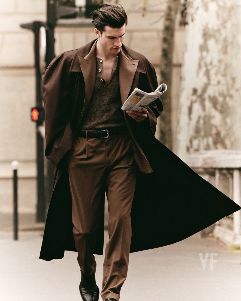 Model Max Knott walking on a city street in a brown coat holding a newspaper for Vanity Fair Italia