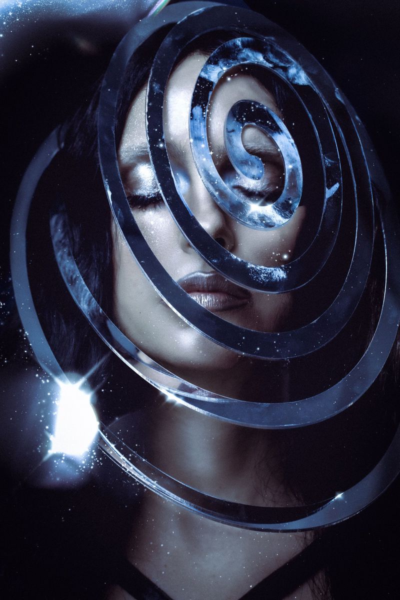 Close-up portrait of a woman framed by metallic spiral rings with shimmering star effects on a dark background.