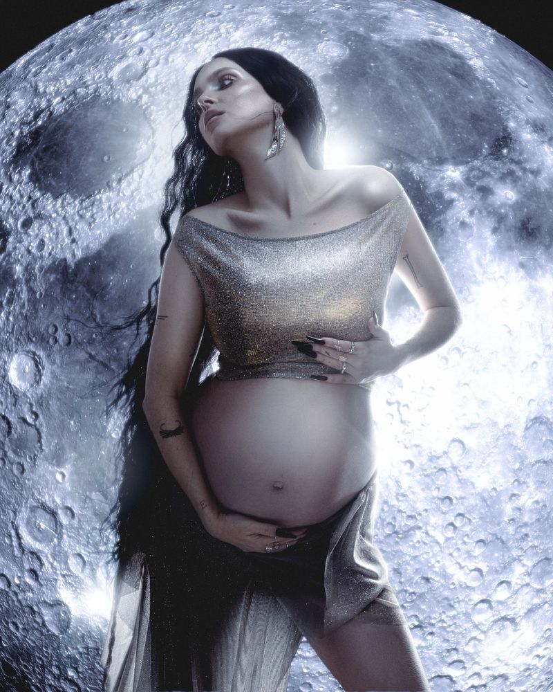 Pregnant woman with long dark hair wearing a metallic top against a detailed moon background for Kaltblut Magazine
