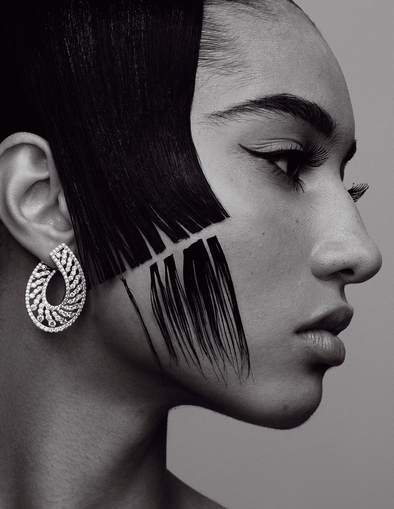 Close-up of a woman's profile with avant-garde hair and makeup in black and white, showcasing dramatic eyeliner and statement earrings.