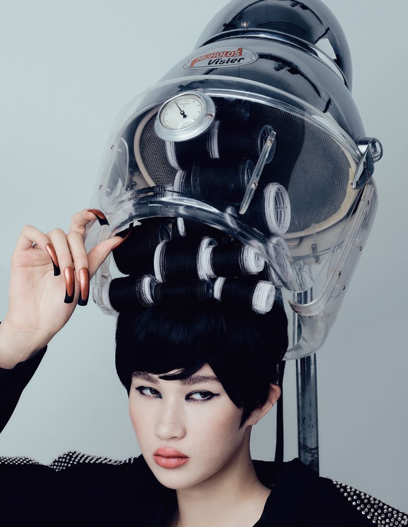 Model wearing black wig under a large clear vintage hair dryer with black and white rollers for Tush Magazine editorial