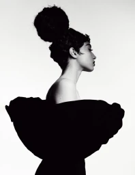 Profile portrait of a model with a voluminous updo hairstyle wearing a sculptural black garment against a white background