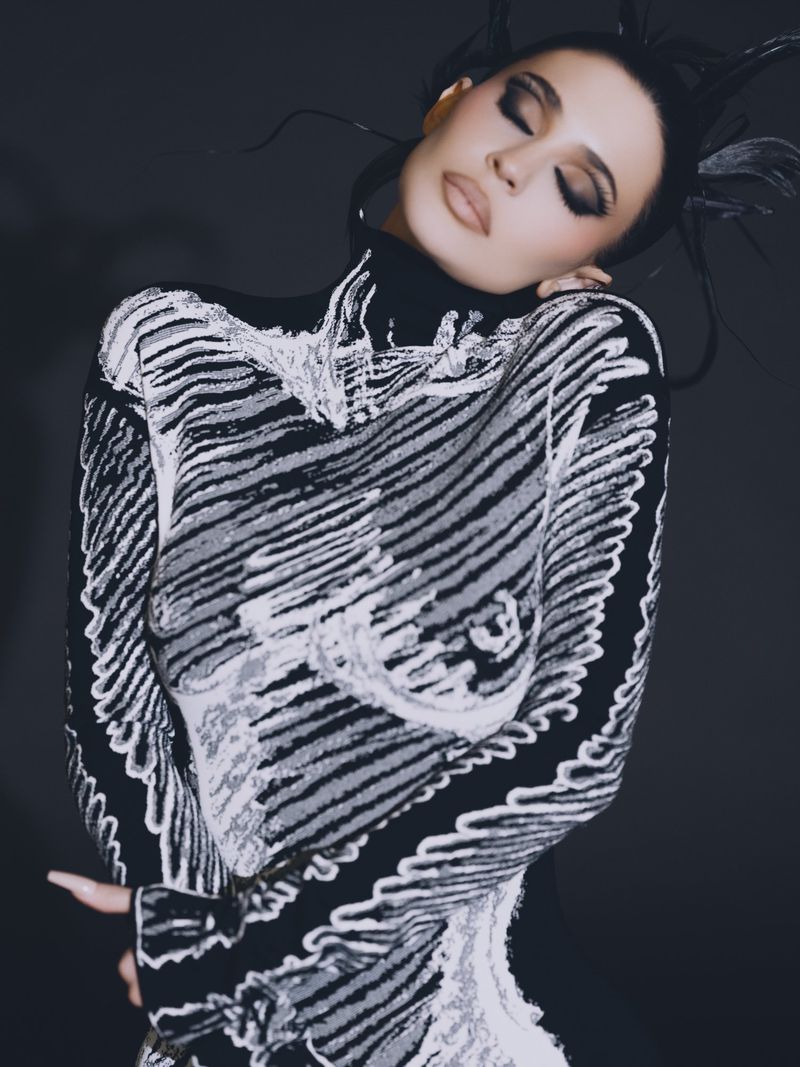 Kylie Jenner wearing a black and white patterned high-neck top with dramatic dark eye makeup against a dark studio background