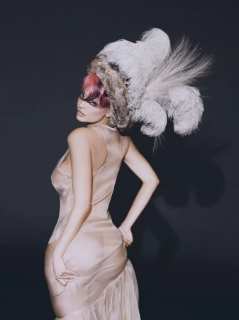 Kylie Jenner wearing a feathered headpiece and sheer gown against a dark background for Puss Puss Magazine