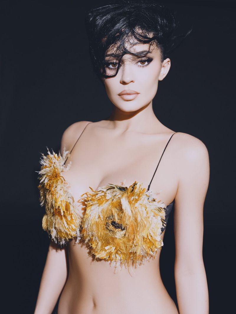 Portrait of a woman with dark hair wearing a feathered top against a dark background in a photo studio environment with studio lighting.