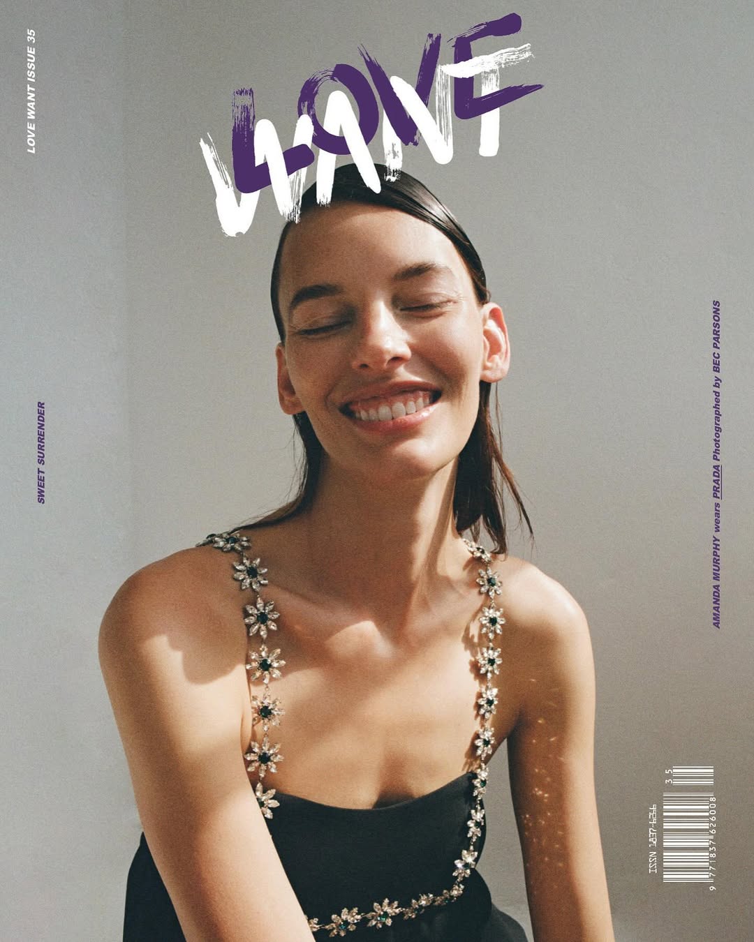 Portrait of a smiling woman wearing a black dress with floral straps, posing in front of a neutral background with magazine typography.