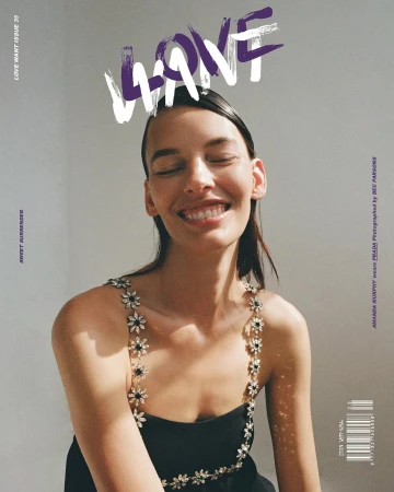 Portrait of a smiling woman wearing a black dress with floral straps, posing in front of a neutral background with magazine typography.
