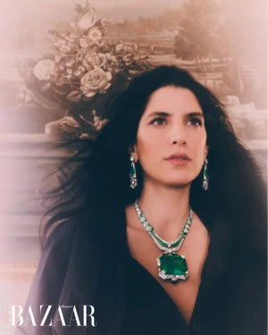 Woman wearing an ornate diamond and emerald necklace and earrings against an antique floral backdrop for Harper's Bazaar Arabia