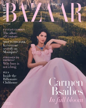Woman in a pink gown with floral details seated among manicured green hedges for a magazine cover.