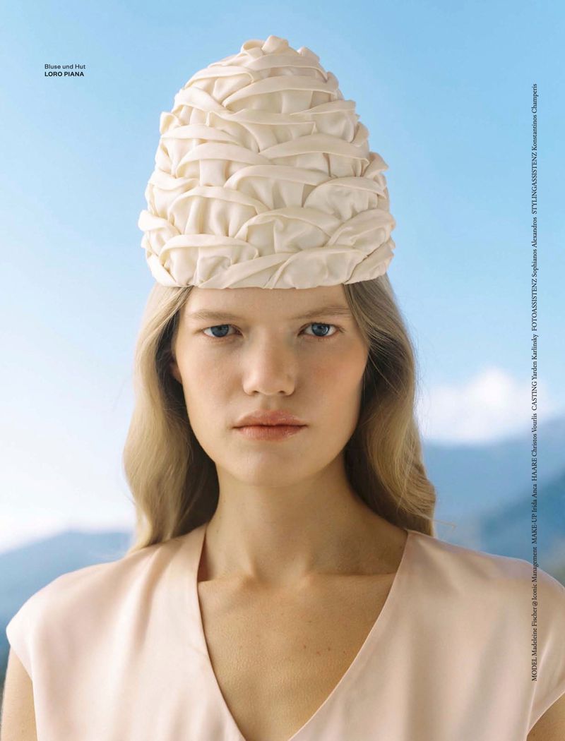 Model wearing a textured cream hat and light-colored top against a blurred mountain backdrop for Flair Germany.