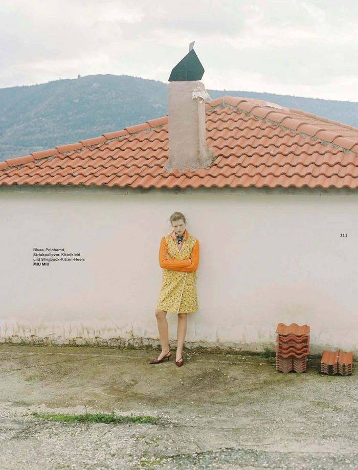 Model leaning against a white wall beneath a tiled roof for a Flair Germany fashion editorial