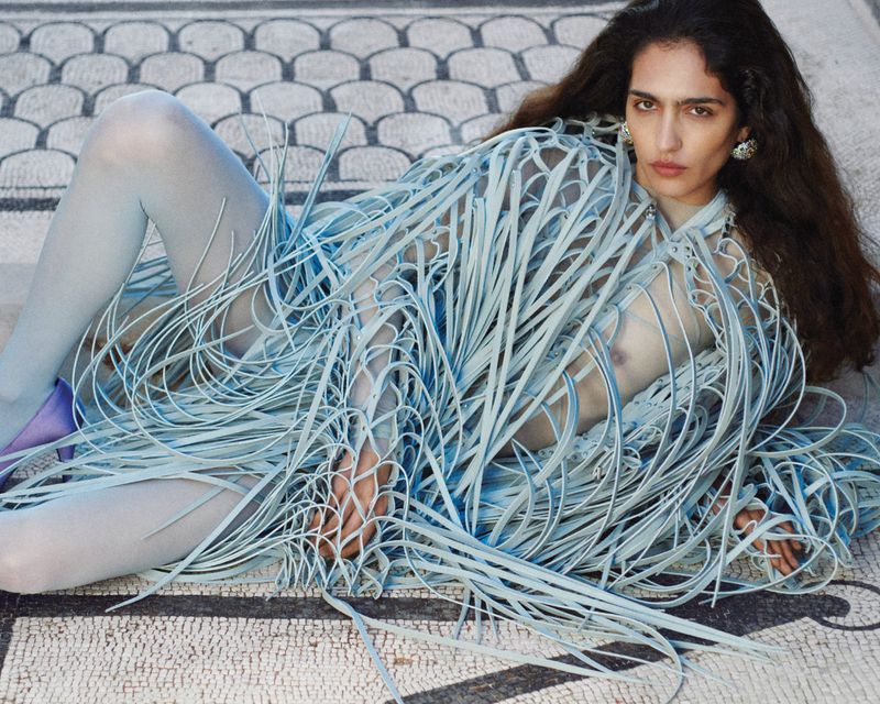 Model lying on a patterned mosaic floor wearing a textured blue fringed top and light blue tights