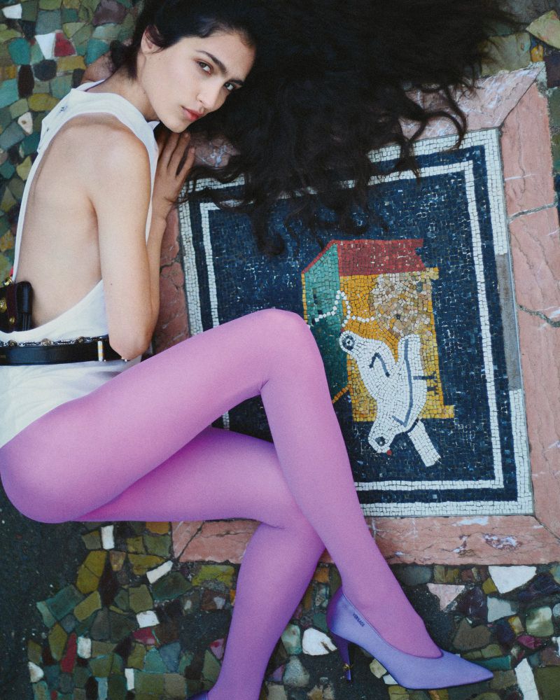 Model lying on an ancient mosaic floor wearing a white top and purple tights for Epoch Review