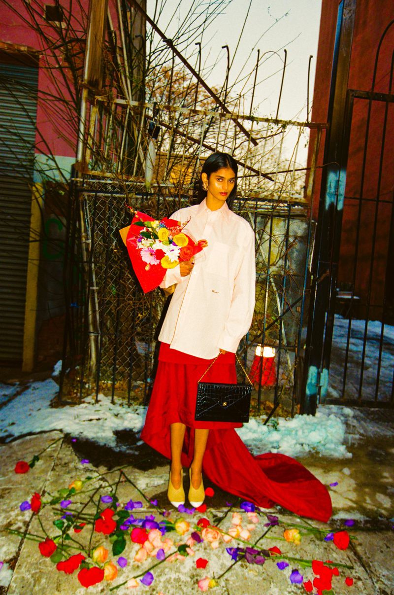 Model Bhavitha Mandava holding a bouquet and black handbag on a city street for The Perfect Magazine editorial.
