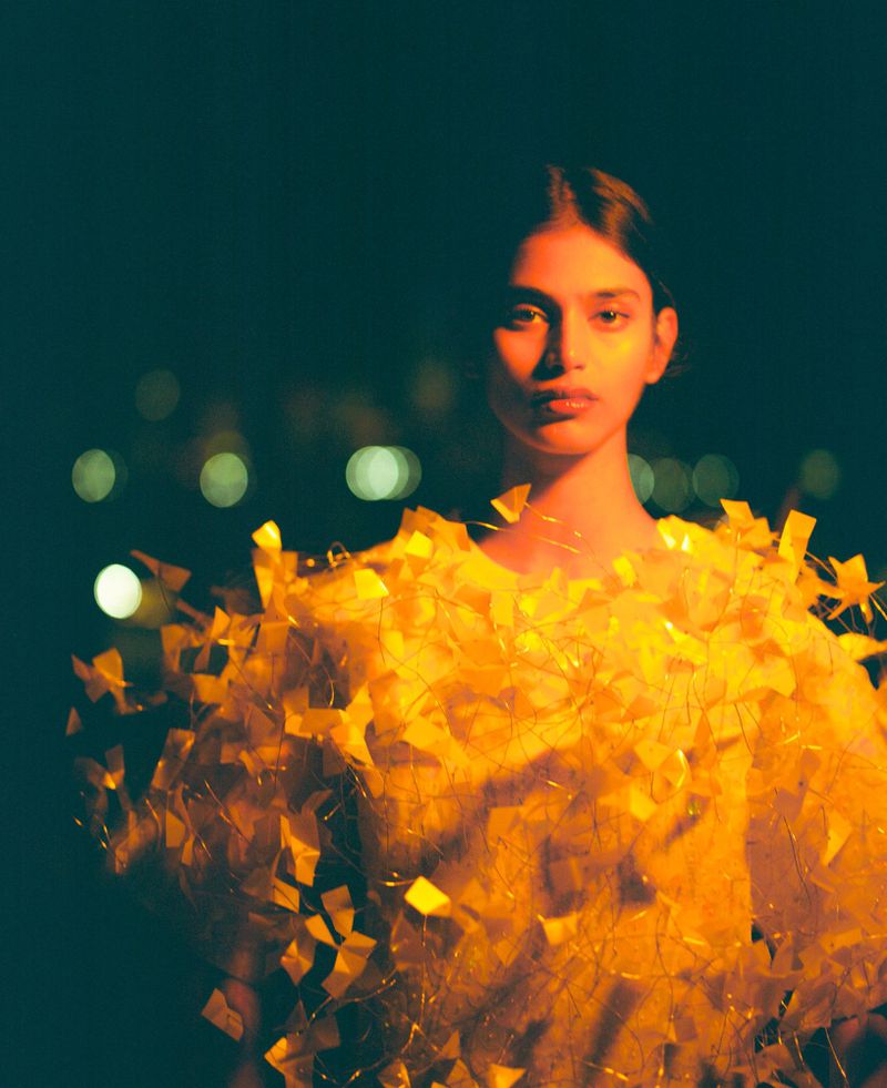 Model Bhavitha Mandava wearing an illuminated yellow garment against a dark nocturnal background for The Perfect Magazine.