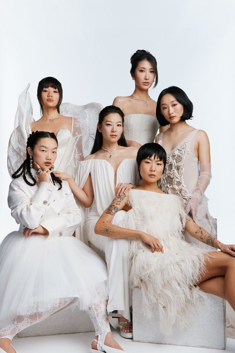 Group of six Asian women in all-white formal wear posing in front of a white background in a studio setting for a fashion editorial.