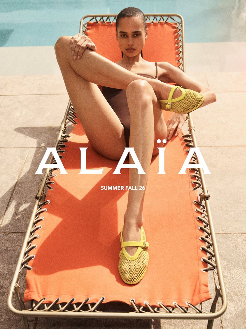 Model relaxing on an orange sun lounger by a pool wearing mesh yellow shoes for Alaïa Summer 2026
