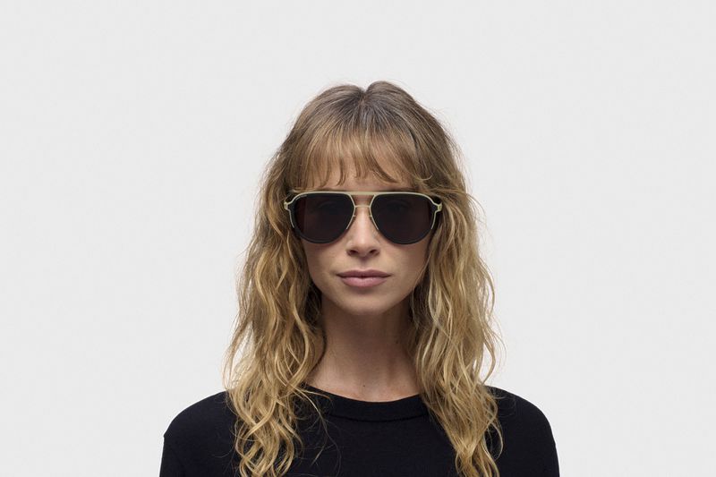 Model wearing dark aviator sunglasses and a black top against a plain white studio background for the RIMOWA X MYKITA collaboration.