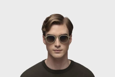 Portrait of a man wearing round sunglasses and a dark crewneck sweater against a clean white seamless studio background.