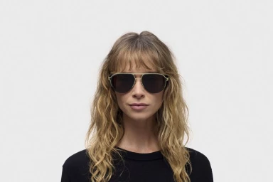 Model wearing dark aviator sunglasses and a black top against a plain white studio background for the RIMOWA X MYKITA collaboration.