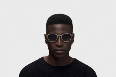 Black man wearing square beige sunglasses and a black sweater against a white seamless background for RIMOWA X MYKITA.
