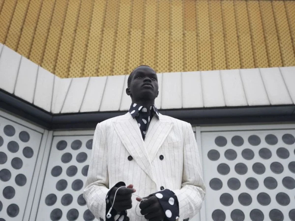 Model wearing a white pinstripe double breasted jacket and polka dot shirt standing against an exterior wall.