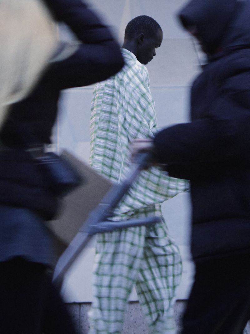 Model Wal Ruop in a green and white plaid suit walking past blurred figures for The Greatest Magazine.