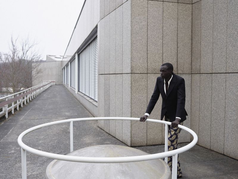Model Wal Ruop in a dark blazer and patterned trousers leaning on a white railing outdoors
