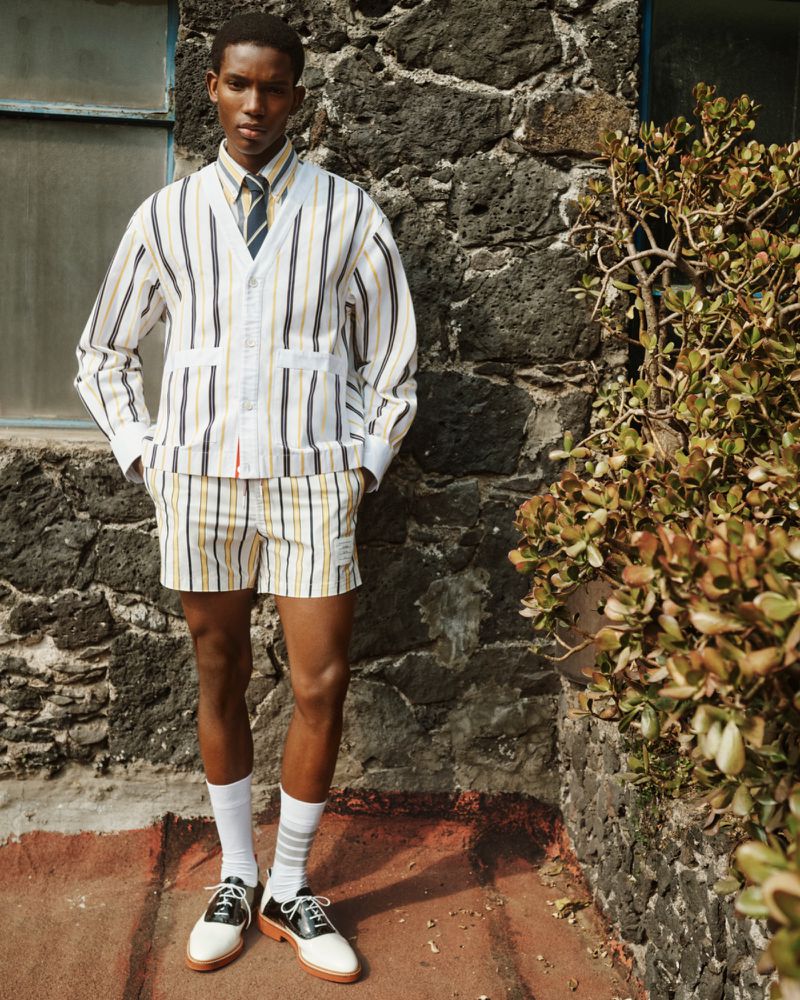 Model wearing a striped cardigan and shorts standing against a stone wall for the Farfetch Lookbook S/S 26