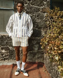 Model wearing a striped cardigan and shorts standing against a stone wall for the Farfetch Lookbook S/S 26