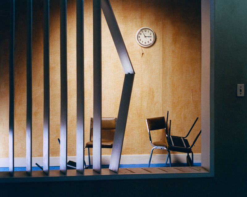 Interior view featuring chairs, an analog clock, and vertical blinds, creating a retro and minimalist aesthetic within a room setting.