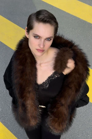 Model in a black top with a brown furry collar looking up against a grey asphalt background with yellow lines.