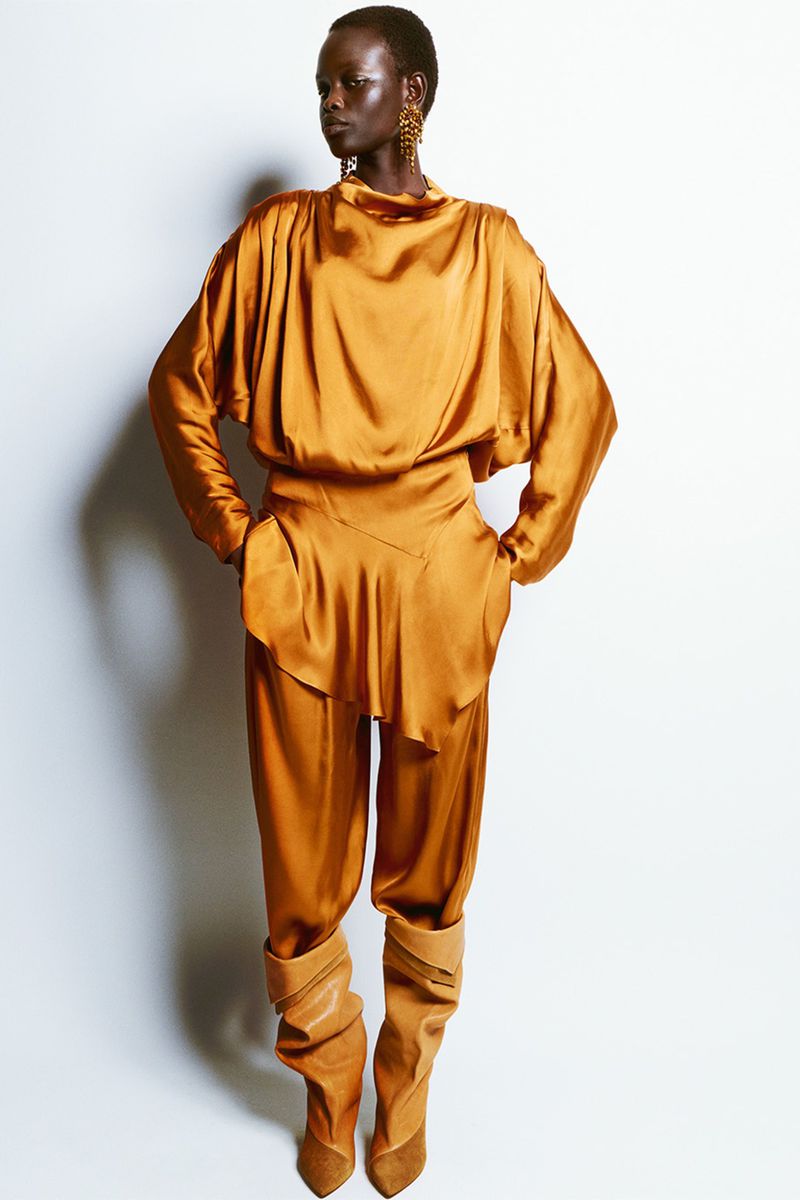 Fashion shot of African woman in a golden blouse and pants with tan colored boots posing against a white background in photo studio.