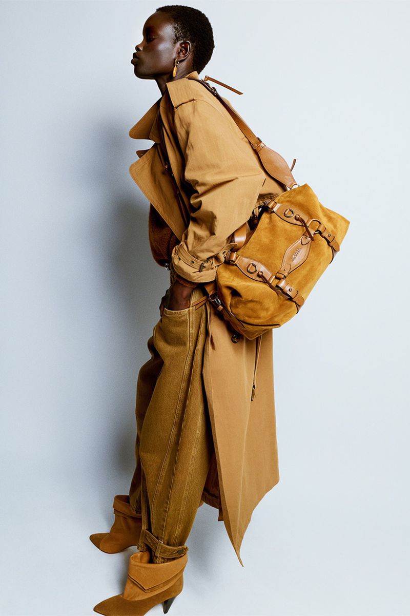 Model in camel coat and suede shoulder bag against a plain light background