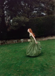 Red-haired female model wearing a flowing green gown running across a green lawn outdoors