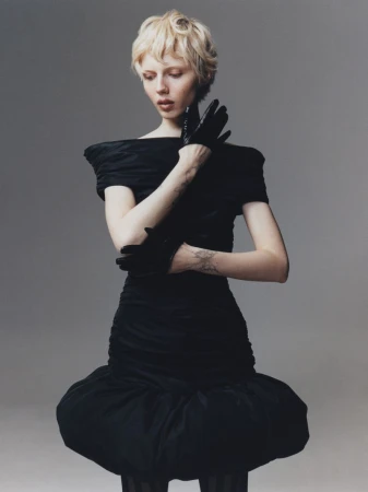 Elegant woman with short blond hair in a black off-the-shoulder dress and gloves posing in a studio, fashion photography.