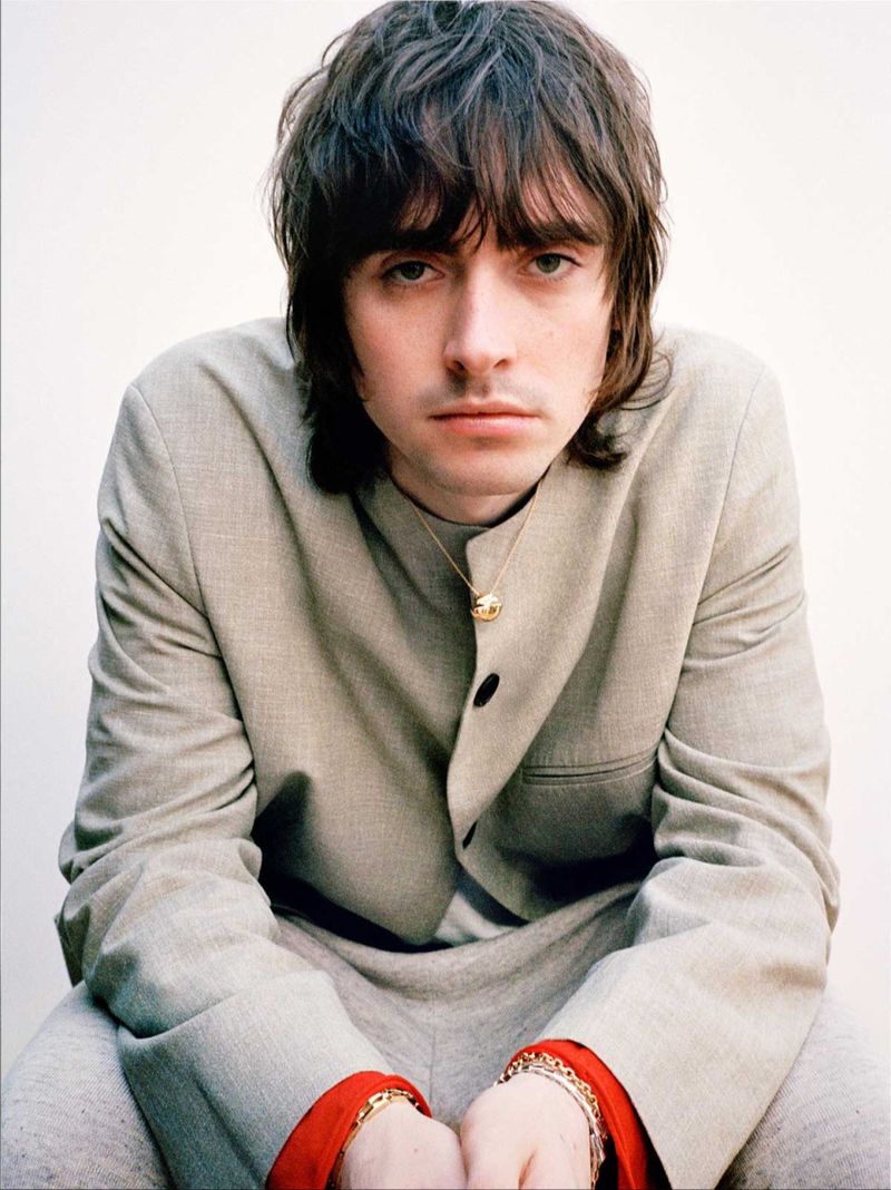 Portrait of a brunette adult male in a grey suit with red sleeve accents, looking directly at the camera against a neutral backdrop.