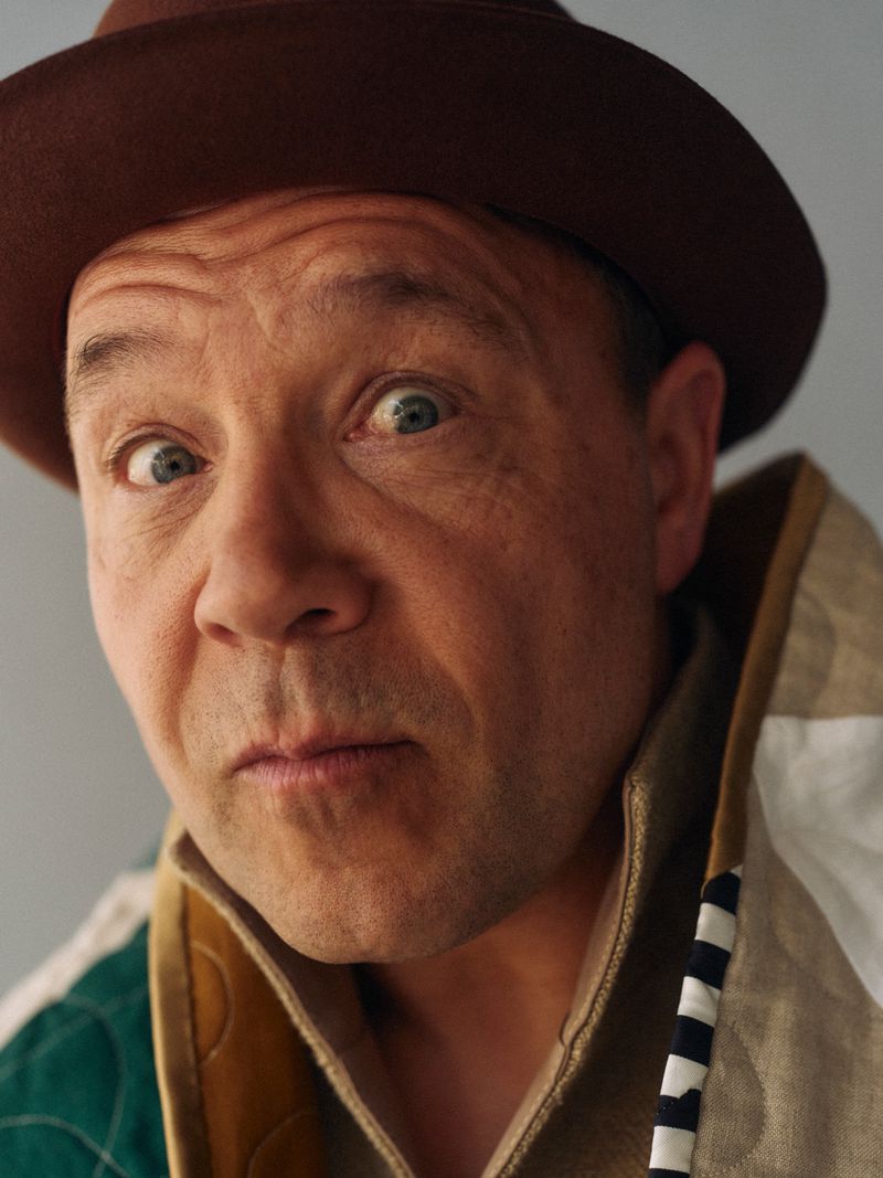 Portrait of a fair-skinned adult male wearing a brown hat and patterned collared jacket looking directly at the camera with a neutral expression.