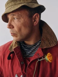 Portrait of a man in a red jacket and bucket hat holding a yellow flower for GQ UK