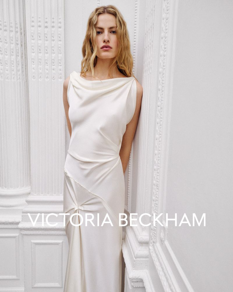 Model Felice Nova Noordhoff in a white silk dress leaning against classical white architectural columns for Victoria Beckham