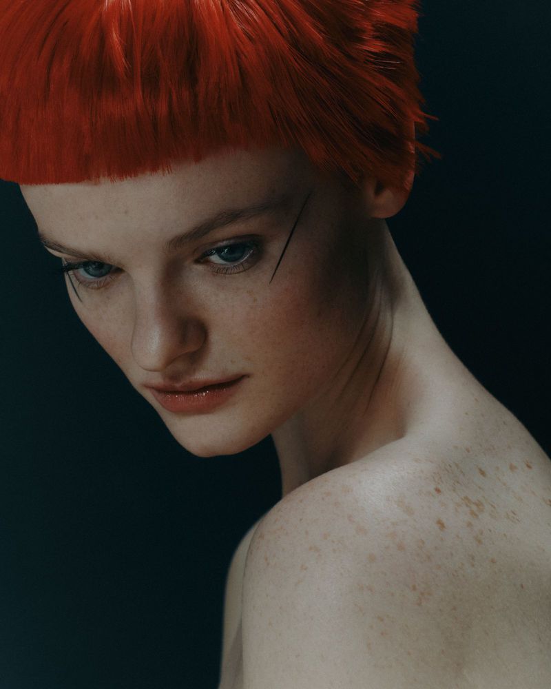 Close-up portrait of a woman with red hair and freckles against a dark background, showcasing fashion and beauty elements.