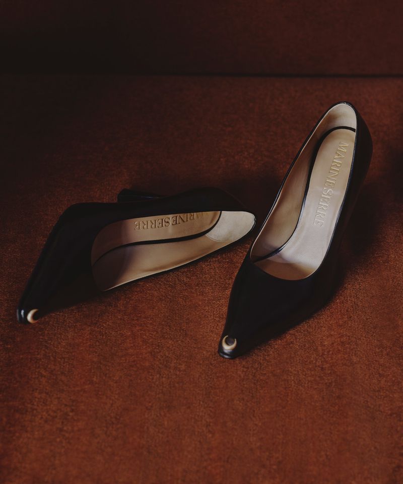 A pair of black pointed-toe heels with gold crescent moon accents resting on a textured brown surface.