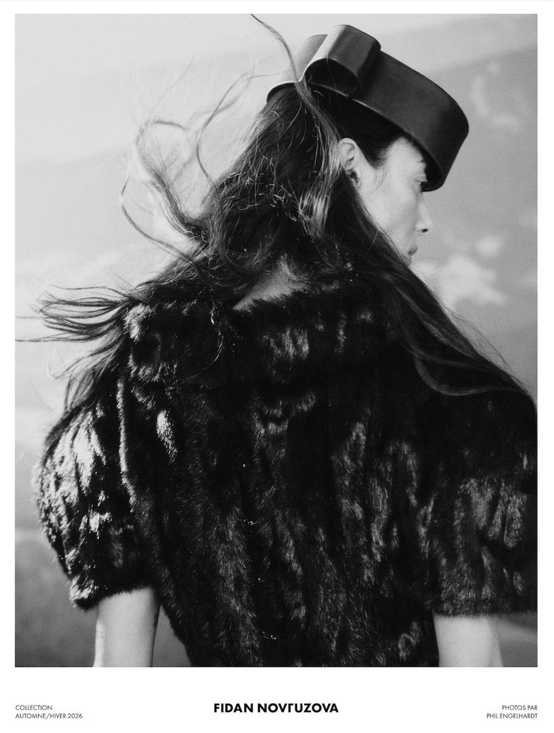 Monochrome fashion campaign image featuring a model wearing a structured dark hat and textured garment against a light background.